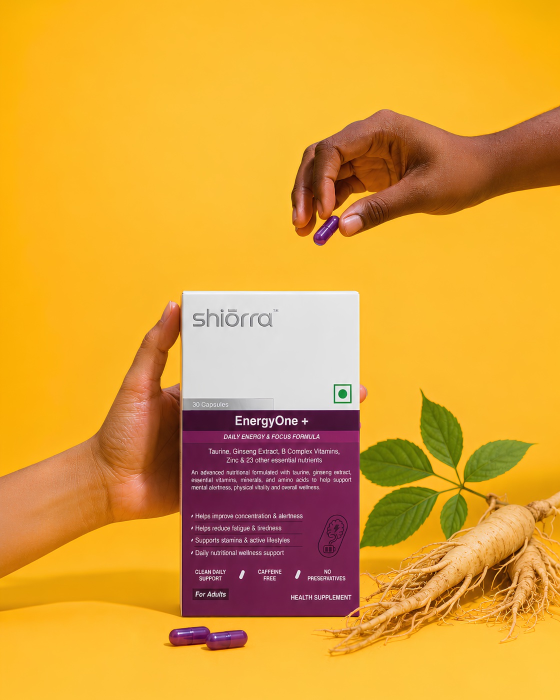 A hand offering a Shiōrra Advanced EnergyOne+ capsule beside the pack and ginseng on a yellow backdrop