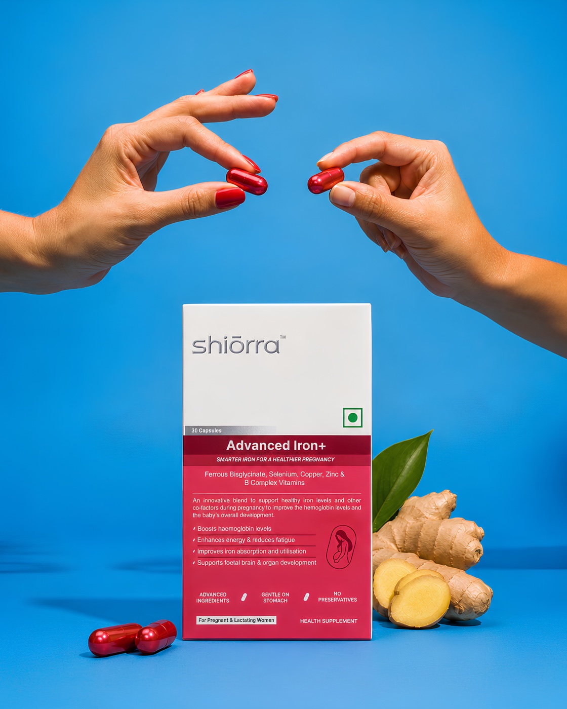 Two hands offering Shiōrra Advanced Iron+ capsules beside the pack and ginger on a blue backdrop